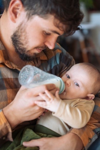 Papa im Karohemd füttert Fläschchen
