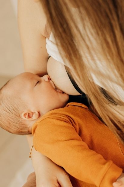 Nahaufnahme eines stillenden Babys mit orangefarbenem Body