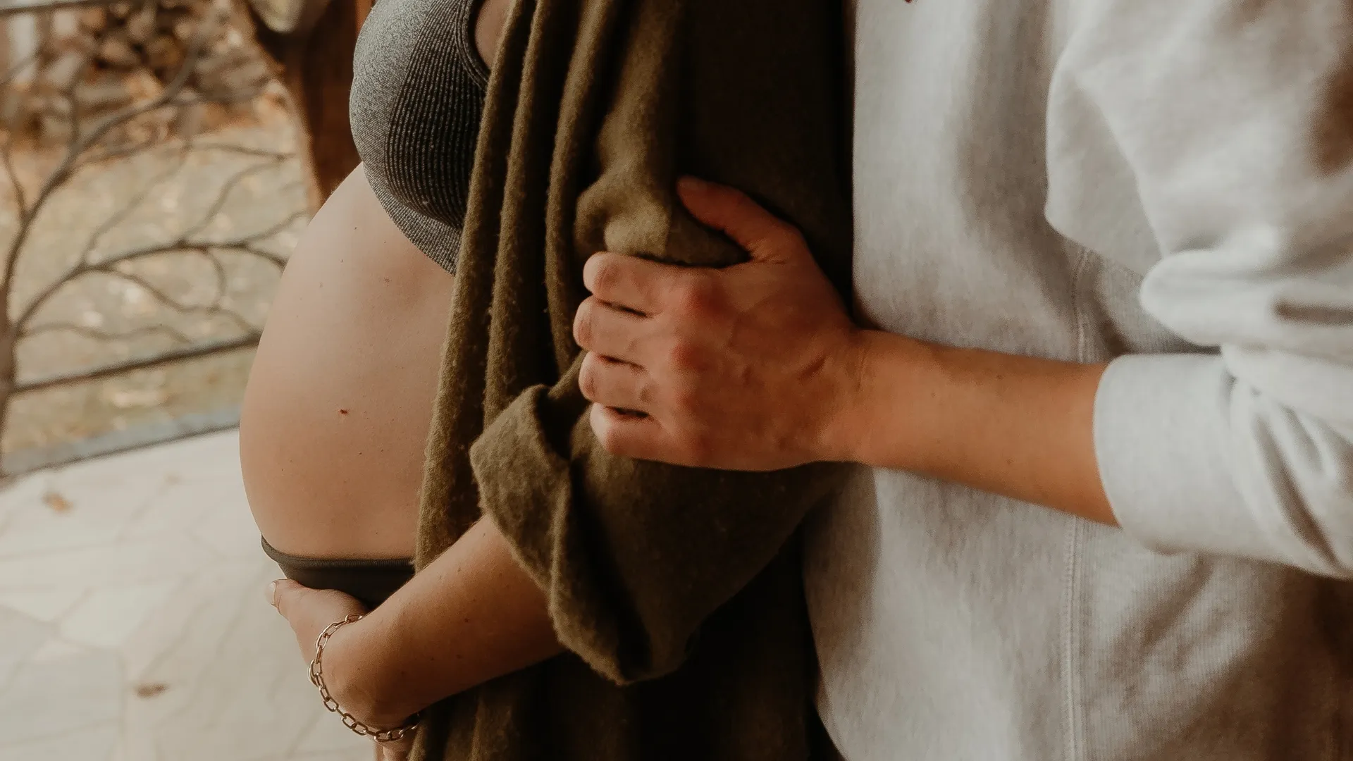 Frau hält ihren nackten Babybauch, während Partner hinter ihr steht und sie im Arm hält